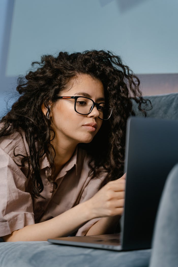 Focused young woman working remotely on her laptop at home, using headphones for a video call.